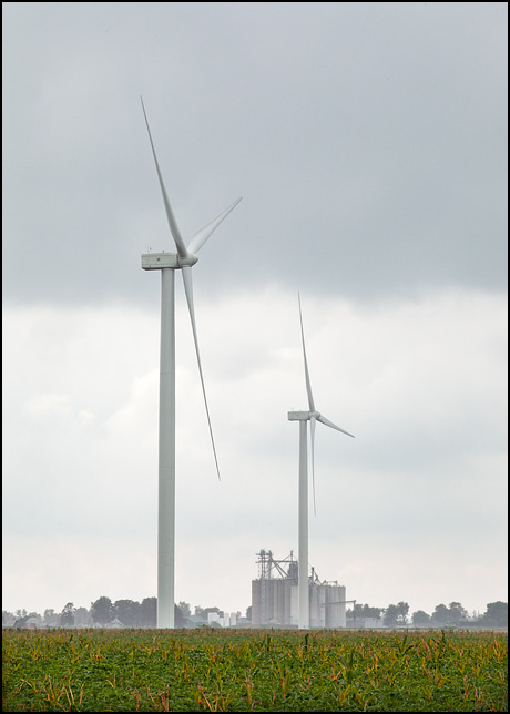 Two wind turbines in a soybean field on a rainy day in Paulding County, Ohio. The grain elevator in the small town of Edgerton, Indiana is visible in the background.