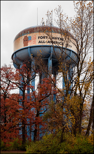 An old rusty water tower on the east side of Fort Wayne, Indiana. The tower has a faded American flag and the title Fort Wayne All-America City painted on it.