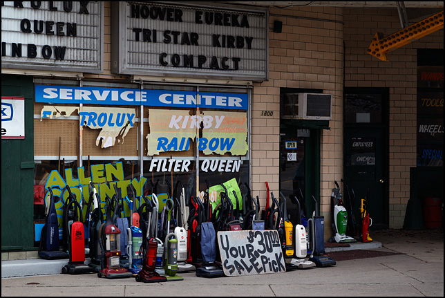 A bunch of used vacuum cleaners stand on the sidewalk in front of the Allen County Sweeper Company on Broadway in Fort Wayne, Indiana.