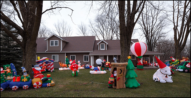 Huge number of inflatable Christmas decorations cover the front yard of a house on Ardmore Avenue in Fort Wayne, Indiana. There is a a Santa house, Santa in a hot air balloon, Santa in an outhouse, a Santa Train, a polar bear, and the red M and M candy man.