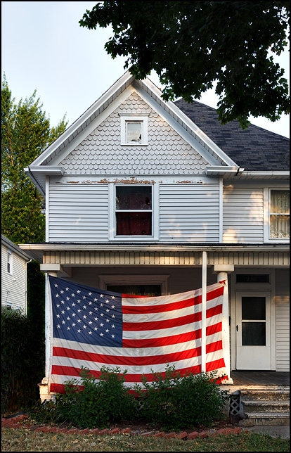 An old Victorian house with a huge American flag covering most of the front porch at the corner of Broadway and Home Avenue in Fort Wayne, Indiana.