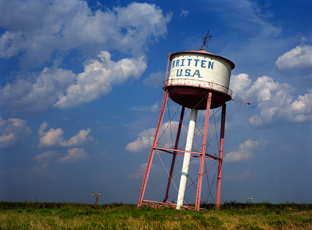 The old Britten USA leaning water tower outside the panhandle town of Groom, Texas on a sunny day with a deep blue sky full of fluffy white clouds.