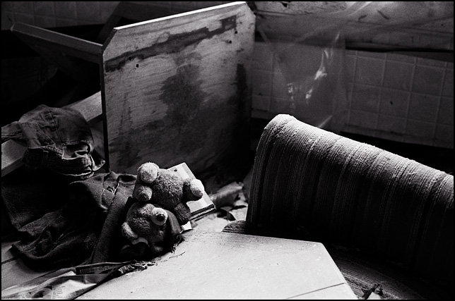 A teddy bear in a pile of broken furniture on the floor of an abandoned house.