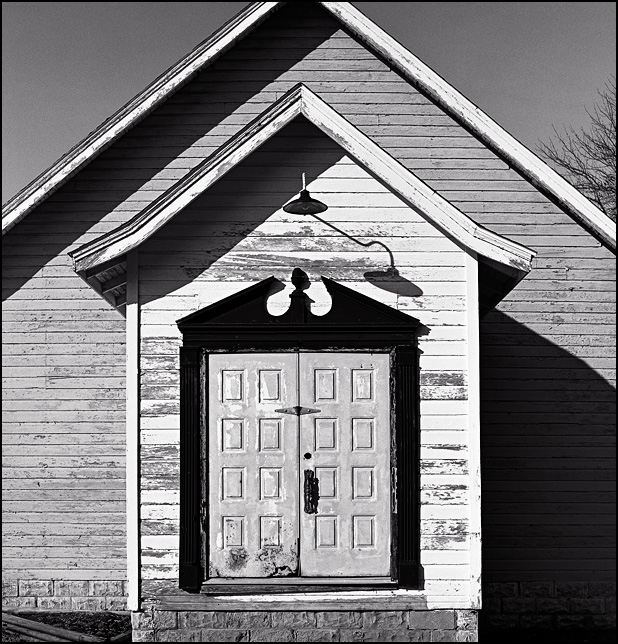 The front of an abandoned church in Edgerton, Indiana. A light casts an unusual shadow above the colonial-style front doors on the weathered building.