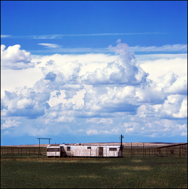 Two old mobile homes in a grassy field under dramatic clouds near the livestock pens on a ranch on US-285 near Encino, New Mexico.