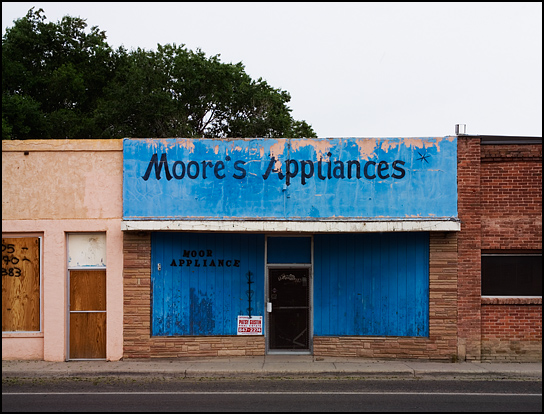 The boarded up storefront of Moore's Appliances in Estancia, New Mexico. Other abandoned stores sit on both sides of it.