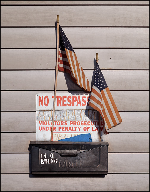 A No Trespassing sign and two American flags hang above a mailbox on the side of an old tenement house in downtown Fort Wayne, Indiana.