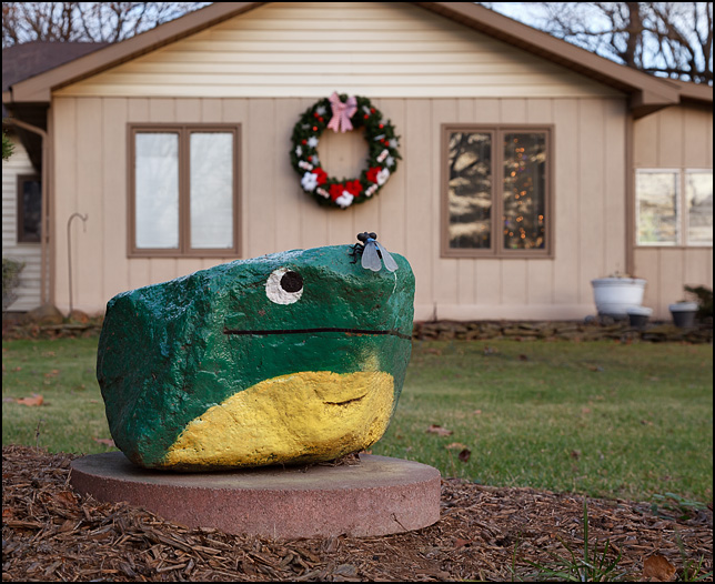 A rock painted to look like a green frog in front of a house on Woodheath Avenue in Fort Wayne, Indiana. It is a miniature copy of the Frog Rock at the Hanson limestone quarry.