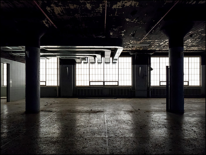 Interior of one of the abandoned industrial buildings in the General Electric factory complex on Broadway in Fort Wayne, Indiana. Several metal ducts on the ceiling vent out through the large frosted glass windows.