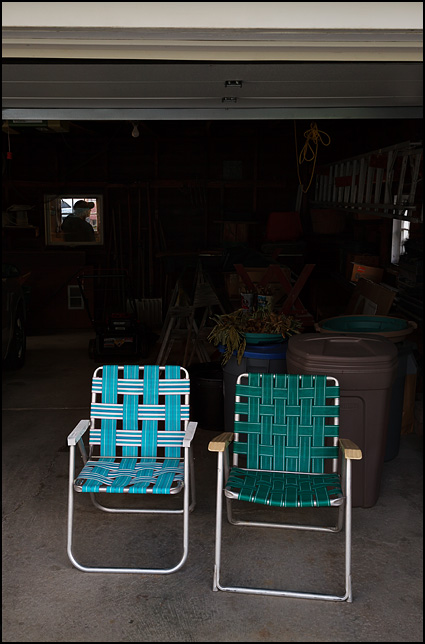 A pair of webbed folding patio chairs sitting side by side in an open garage door.