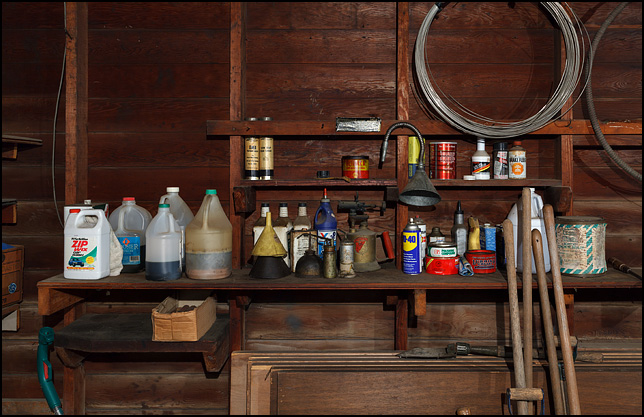 A wooden shelf full of old oil cans, bottles of motor oil, and jugs of automotive fluids in my grandpas old garage.