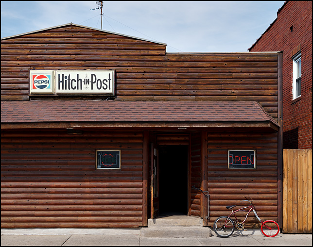 An old bicycle with a wooden front wheel leans against the front of the Hitch-In-Post tavern on High Street in Fort Wayne, Indiana.