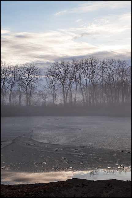 The sun rises on a foggy morning over the pond at Hodell Acres, the WMCA summer camp on Elmhurst Drive in Fort Wayne, Indiana. The surface of the pond is covered in a thin layer of ice.