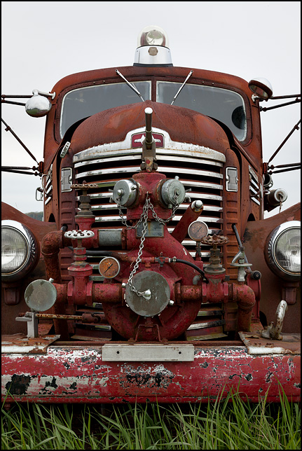 The front of an abandoned late 1940s International KB-7 fire truck, showing the grille and the pumping equipment mounted on the it.