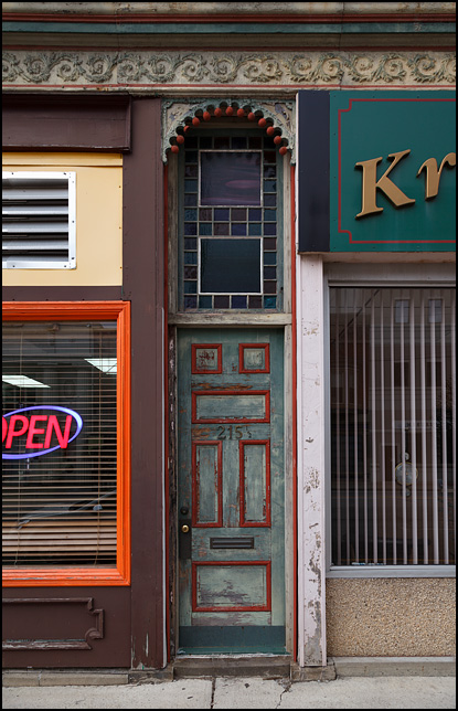 A colorful door with an intricately decorated archway above it between two storefronts in a building on Main Street in the small town of Kendallville, Indiana.