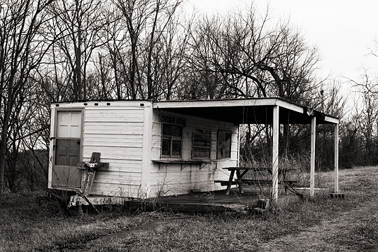 An abandoned hotdog stand on Old Louisville Road in rural Spencer County, Kentucky with a memorial cross leaning against the end of the trailer.