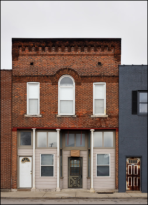 An old vacant brick storefront building on South Street in the small town of Monroeville, Indiana. The second floor has an arched window in the middle.
