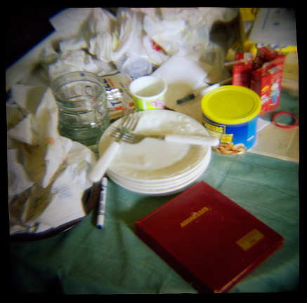 Dirty dishes and a red address book on the kitchen table, photographed with a Diana toy camera.