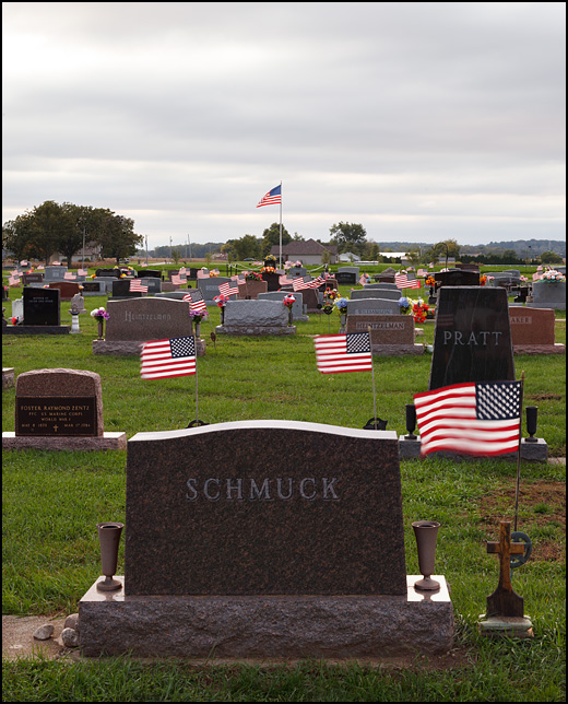 Small American flags fly from all of the tombstones at Sparta Cemetery in the small town of KImmell, Indiana. The name on the tombstone in the foreground is Schmuck.