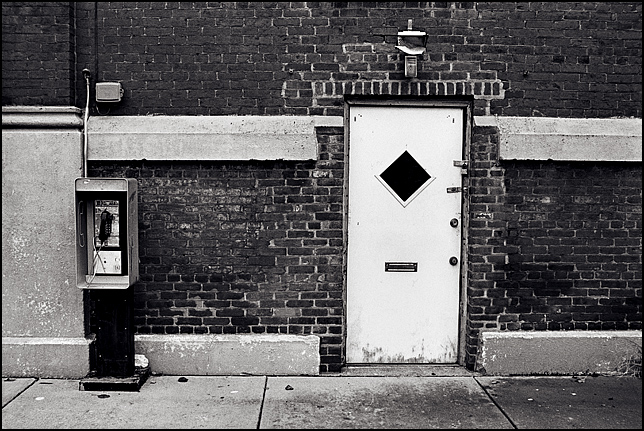 A payphone stands next to a door with four locks on it in the side of a rundown brick building along Shelby Street in downtown Louisville, Kentucky.