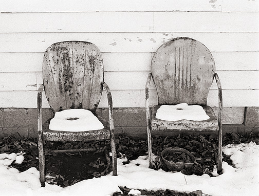 Snow covers a pair of rusty old metal motel chairs next to an old man's house in rural Allen County, Indiana.