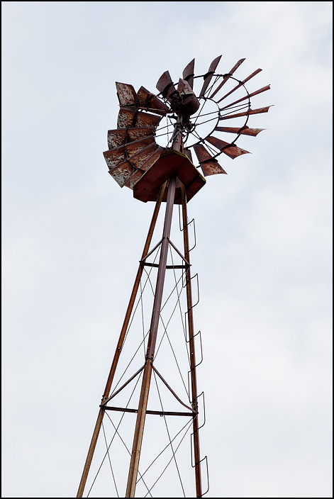 An old rusty windmill stands on top of a tall steel lattice tower on a farm on State Road 37, near the state line, in rural northeast Allen County, Indiana.
