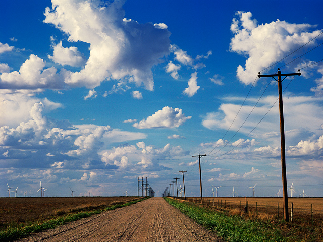 Everett Road stretches into the distance toward a wind farm under a cloud filled blue sky in Oldham County, Texas.
