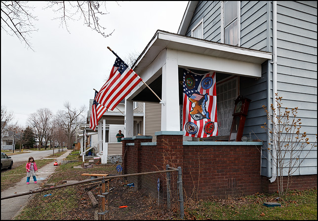 A house with three American flags on the porch. One has the insignia of all the branches of the US Military and the POW-MIA flag on it.