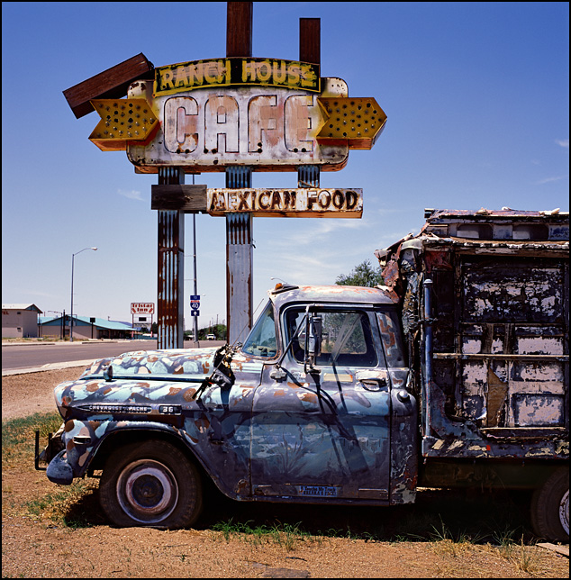 An old beat-up Chevrolet pickup truck with a homemade camper shell sits in front of a sign for the abandoned Ranch House Cafe Mexican Restaurant on Route 66 in Tucamcari, New Mexico.