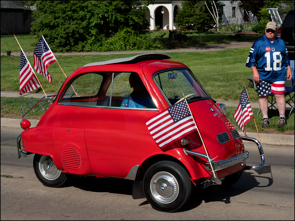 A man watches a red 1957 BMW Isetta 300, decorated with American flags, drive past during the 2023 Waynedale Memorial Day Parade in the Waynedale area of Fort Wayne, Indiana.