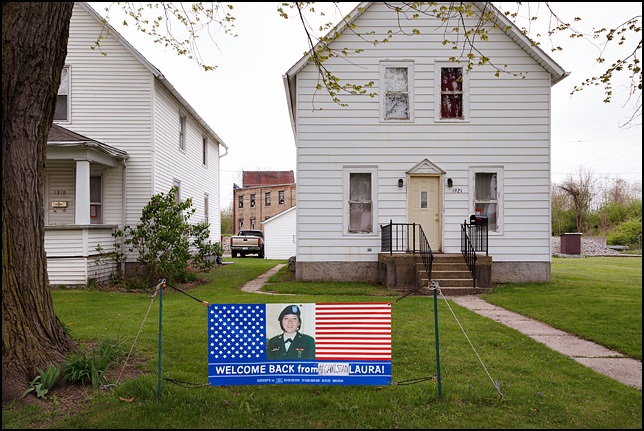 An American flag banner in the front yard of a house on West Main Street in Fort Wayne, Indiana. The banner has a photo of army veteran Laura Bonano and the message, Welcome Home From Afghanistan Laura.