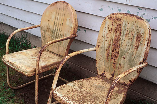 Two rusty old yellow metal motel chairs next to grandpas house.