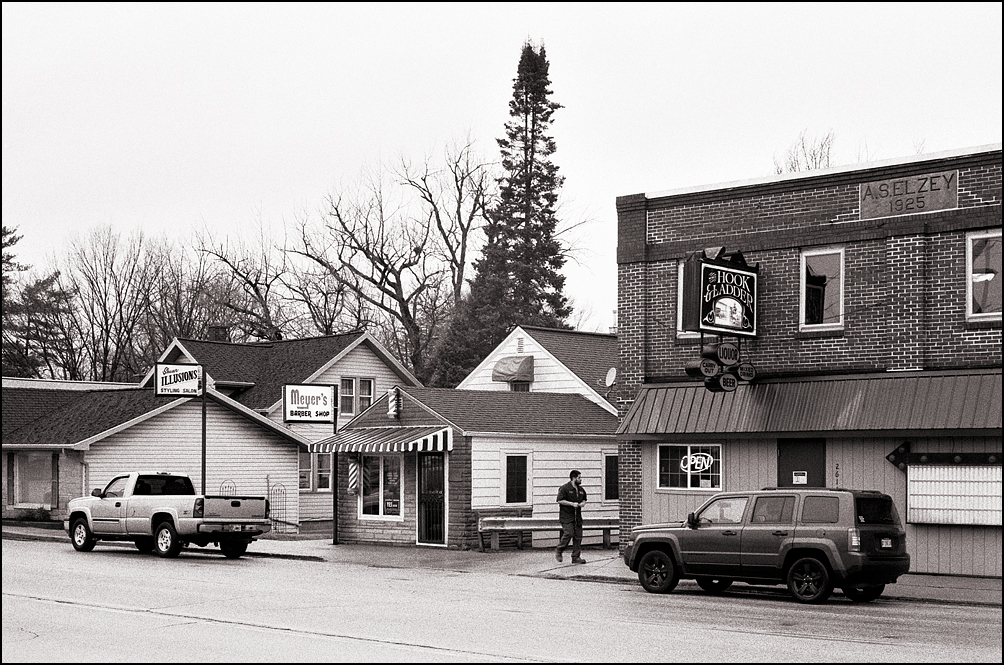 The Imel Insurance building, Meyers Barber Shop and The Hook and Ladder Tavern on Lower Huntington Road in the Waynedale area of Fort Wayne, Indiana. A man is walking from the barbershop to his car.
