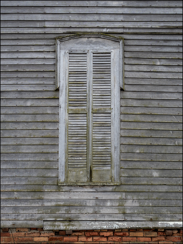 A window covered with weathered wooden shutters on an abandoned farmhouse on US-421 in rural LaPorte County, Indiana.