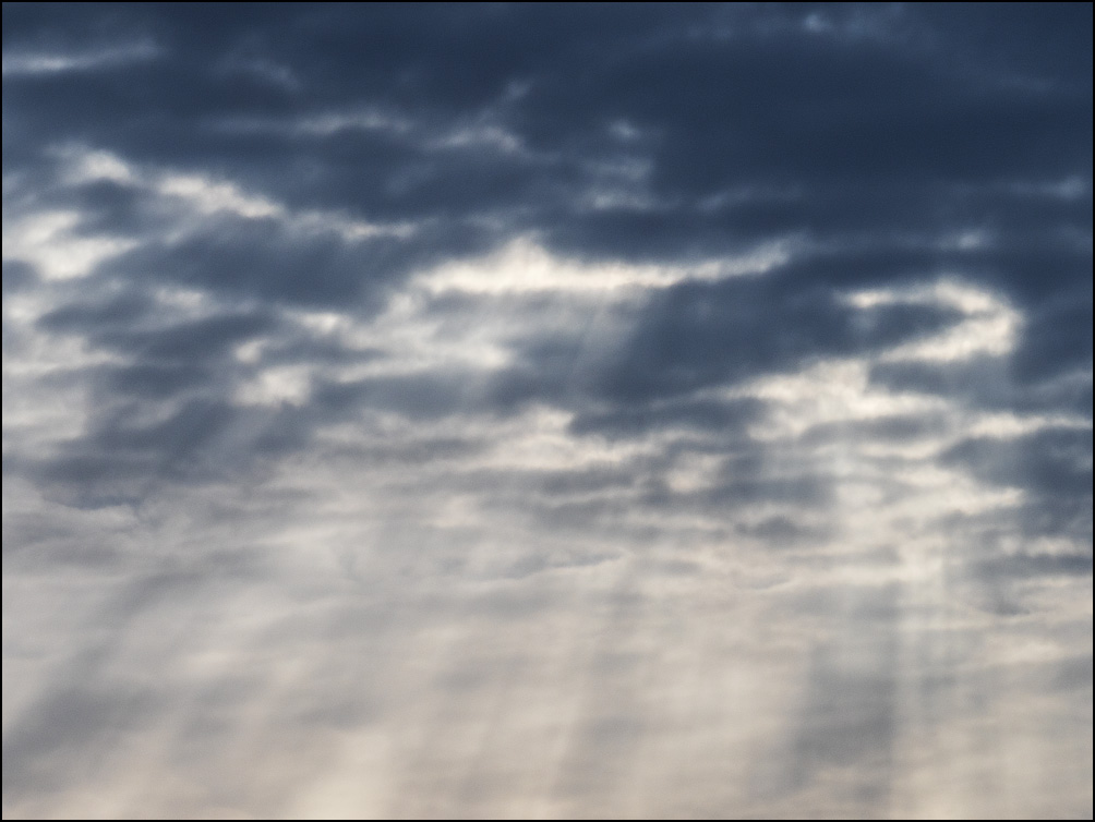 An abstract photograph of rays of light streaming out from the bottom of a large dark cloud bank in the morning sky over Fort Wayne, Indiana.
