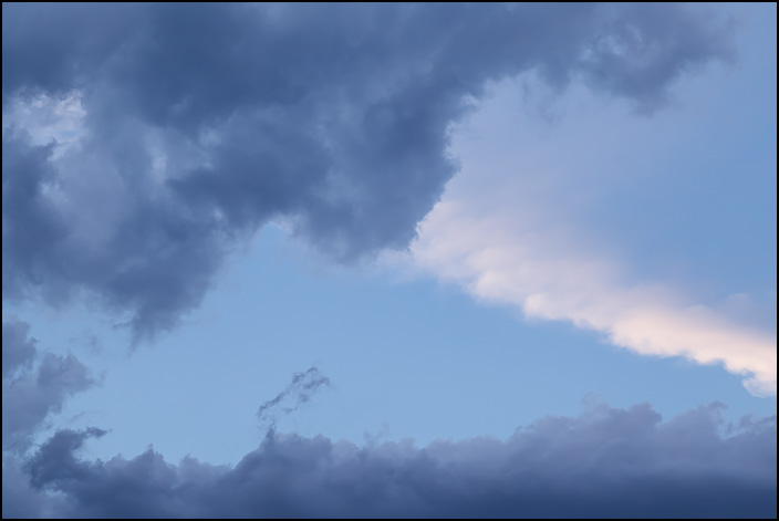 An abstract photograph of dark clouds surrounding a spot of blue sky on a June evening in the small town of Churubusco, Indiana.