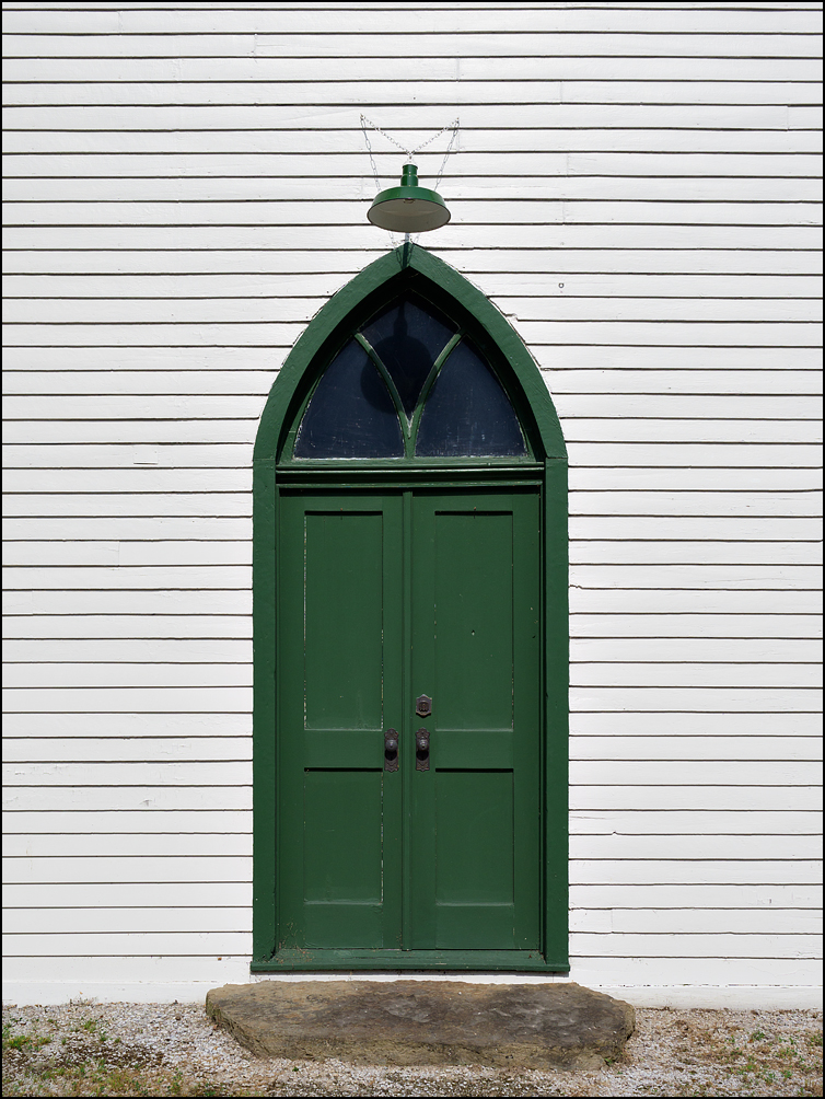 The green double doors and gothic-arch window on the front of the old white church at the Prairie Grove Cemetery in the Waynedale area of Fort Wayne, Indiana.