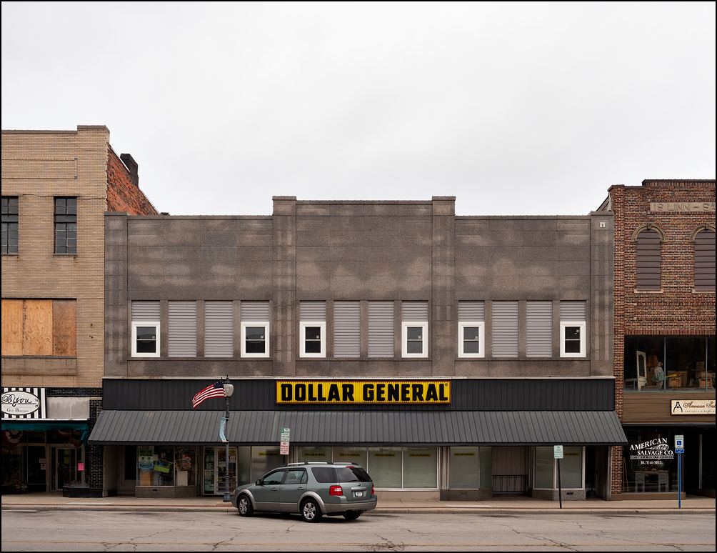 A Dollar General store in a former Morris 5 and 10 storefront on Market Street in the small town of Bluffton, Indiana. An American flag flies from a lamp post in front of the building.