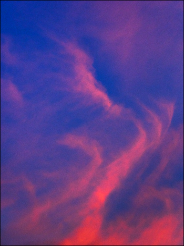Abstract photograph of swirling red clouds in a deep purple sky in the early morning.