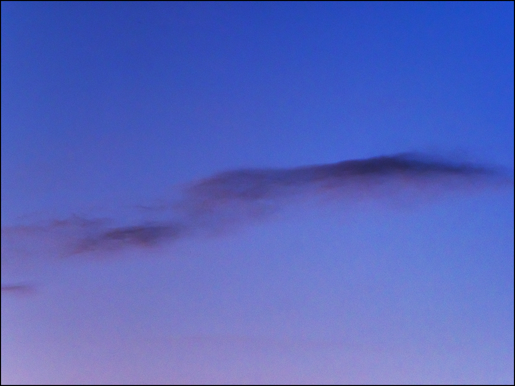 Abstract photograph of a dark band of clouds in a deep purple sky in the early morning.