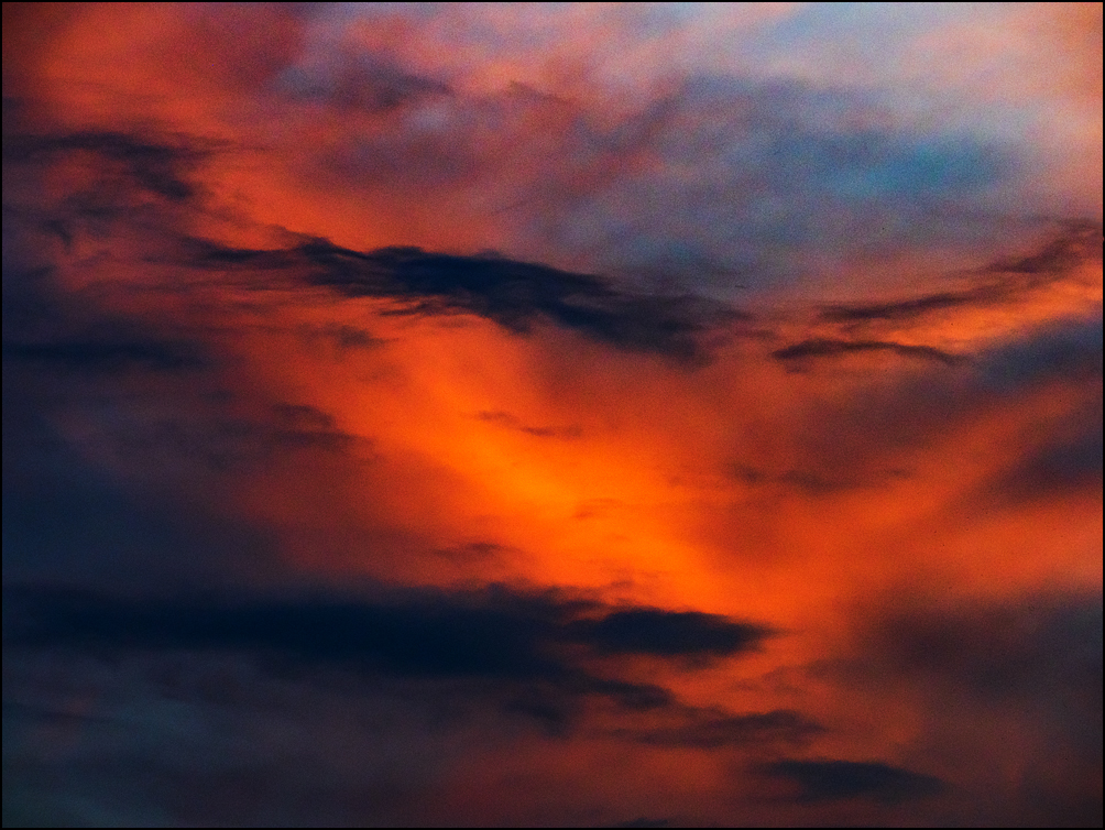 Abstract photograph of a band of orange light surrounded by dark clouds in the early morning soon after sunrise.