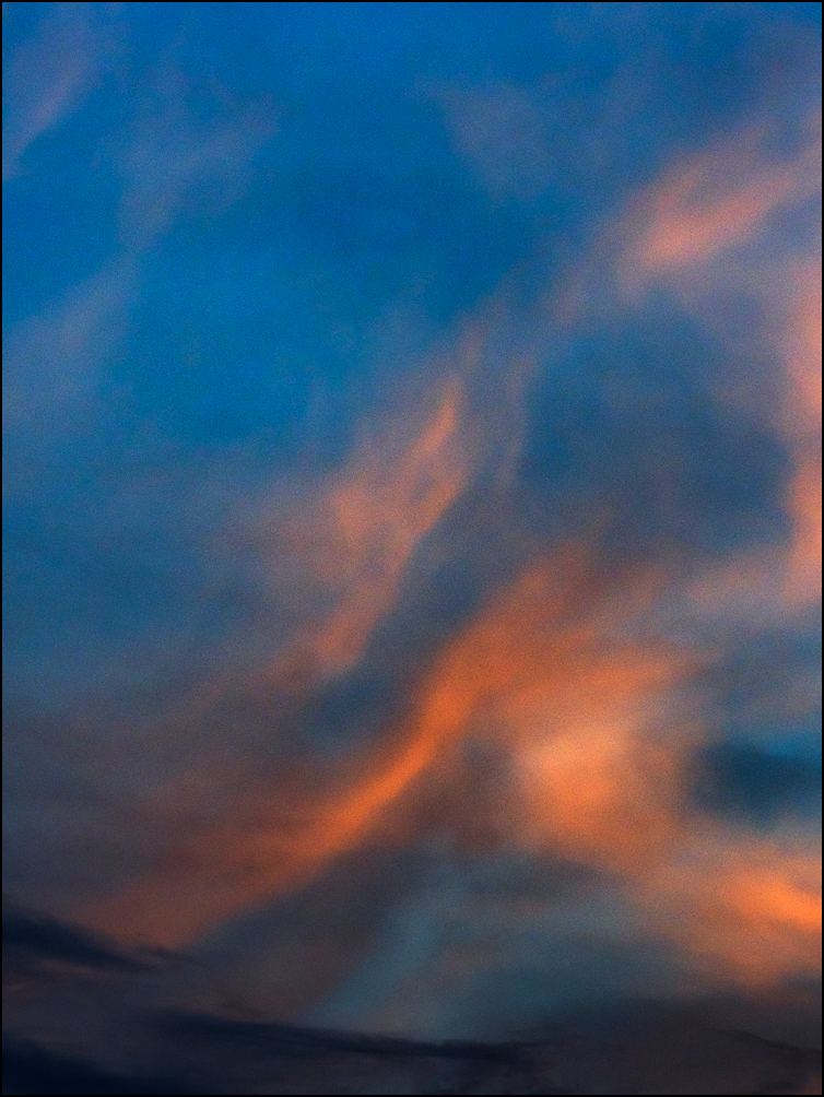 Abstract photograph of bands of orange clouds arching up into a blue sky from a dark cloud below.