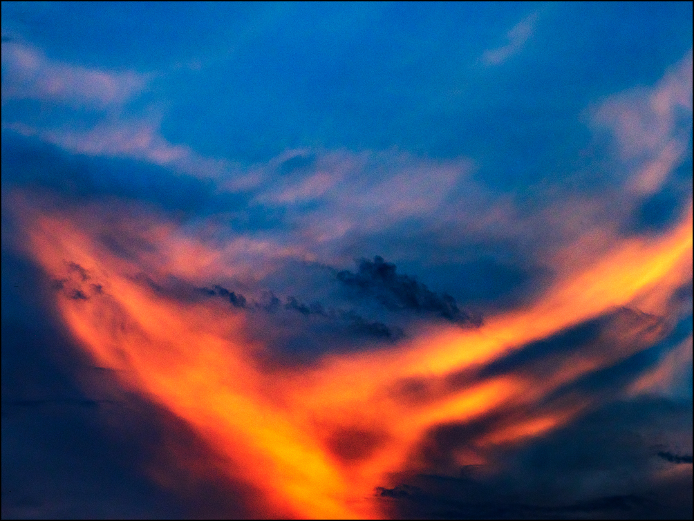 Abstract photograph of chevron of orange light streaking across a dark blue sky at sunrise.