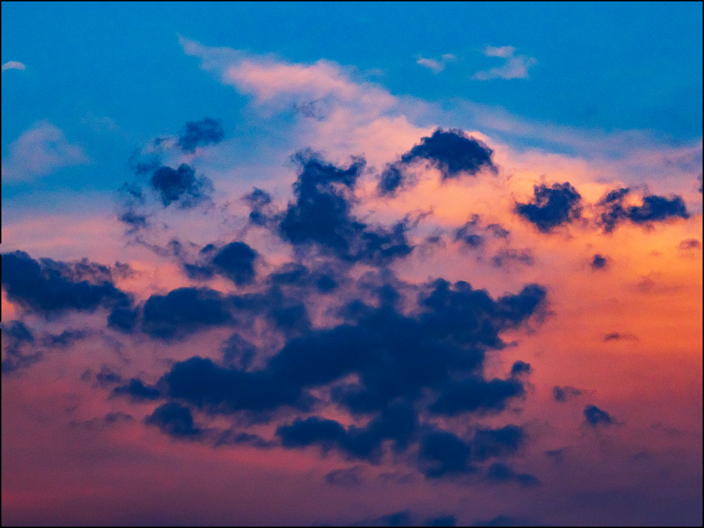 Abstract photograph of dark purple clouds surrounded by a ring of orange clouds in a light blue sky at sunrise.