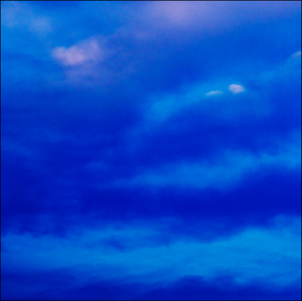 Abstract photograph of horizontal bands of dark blue clouds in a light blue evening sky in July.
