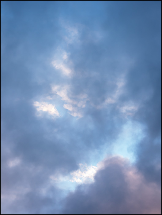 An abstract photograph of dark summer storm clouds breaking up to reveal a blue sky in the early morning over Fort Wayne, Indiana.