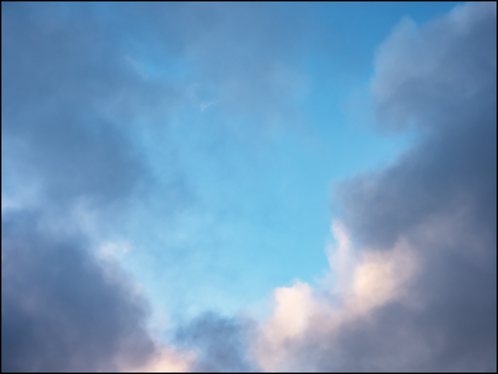 An abstract photograph of a blue sky and white clouds surrounded by dark clouds after the rain in the early morning over Fort Wayne, Indiana.