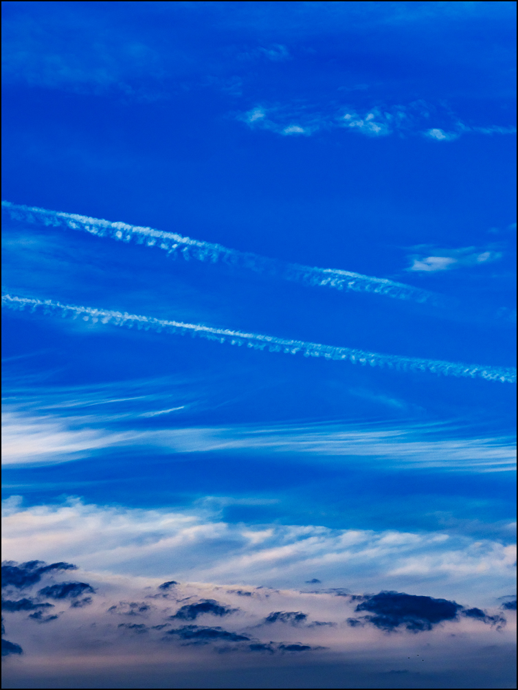 Abstract photograph of bands of white clouds in a deep blue sky over a line of small dark clouds.