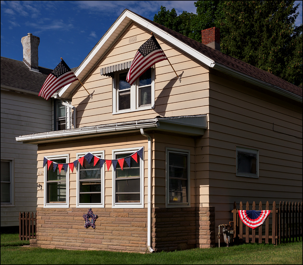 A house covered in patriotic decorations on Wells Street in Fort Wayne, Indiana. It has two American flags, a tinsel star, and bunting.