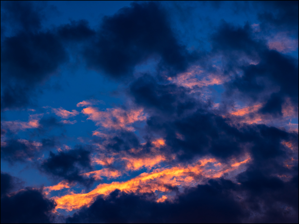 An abstract photograph of bands of orange light surrounded by dark clouds in the morning sky over Fort Wayne, Indiana.